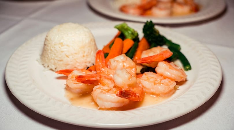 Shrimp, white rice, and colorful steamed vegetables served on a white plate.